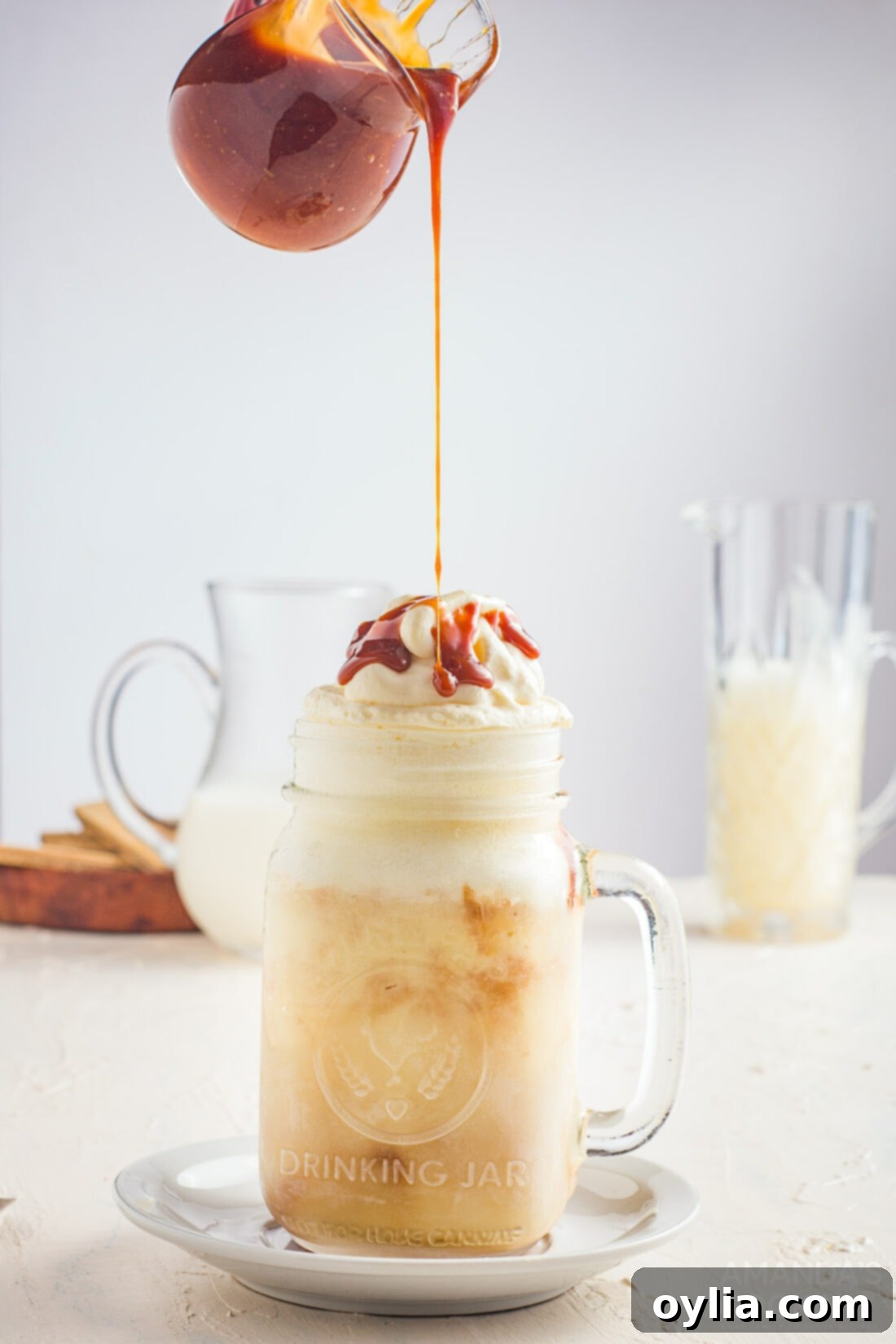 A hand drizzling rich salted caramel sauce over a freshly blended milkshake, topped with fluffy whipped cream.