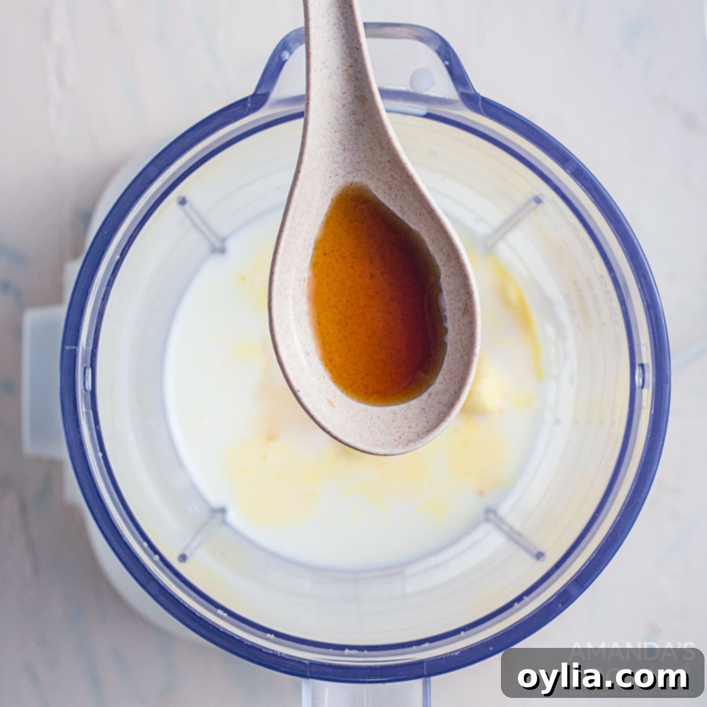 A spoon with salted caramel sauce poised over a blender with a creamy milkshake mixture, ready for topping.