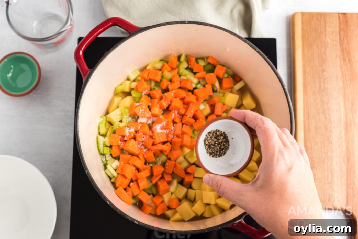 A saucepan filled with potatoes, carrots, celery, chicken broth, and pepper, simmering on the stovetop.