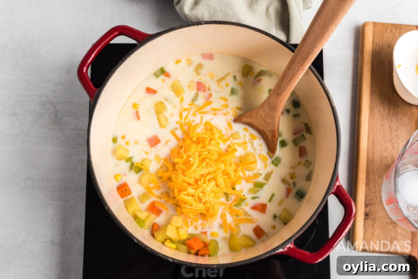 Milk and shredded cheese being stirred into a saucepan of corn chowder soup.