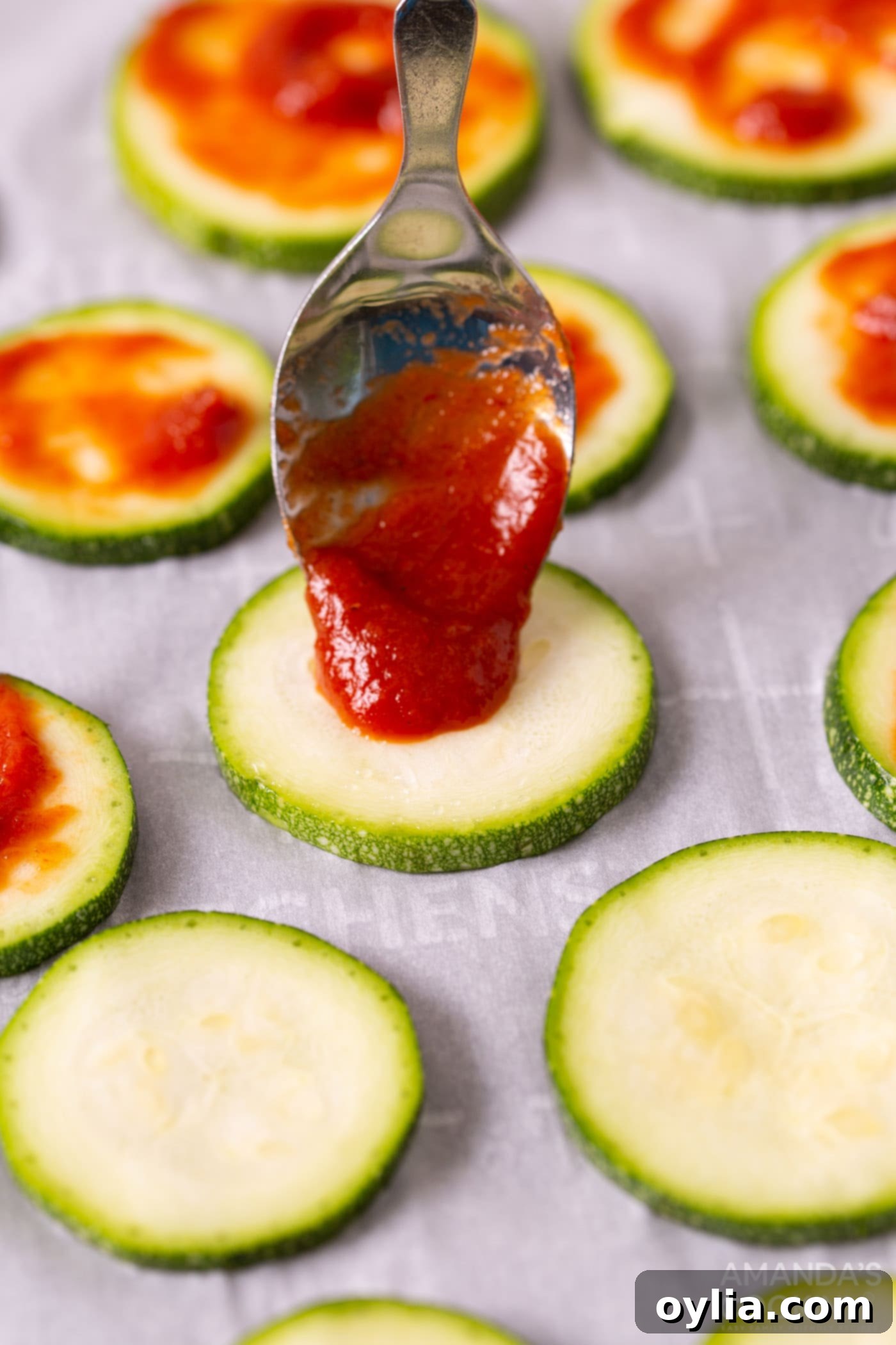 spoon pouring pizza sauce onto zucchini slice