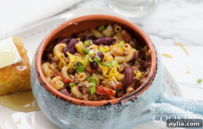 A beautifully presented bowl of Chili Mac, accompanied by a slice of warm cornbread drizzled with honey, highlighting a perfect comfort meal.