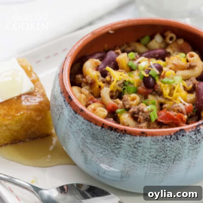 A generous serving of Chili Mac in a white bowl, with a golden square of cornbread beside it, ready for a comforting meal.