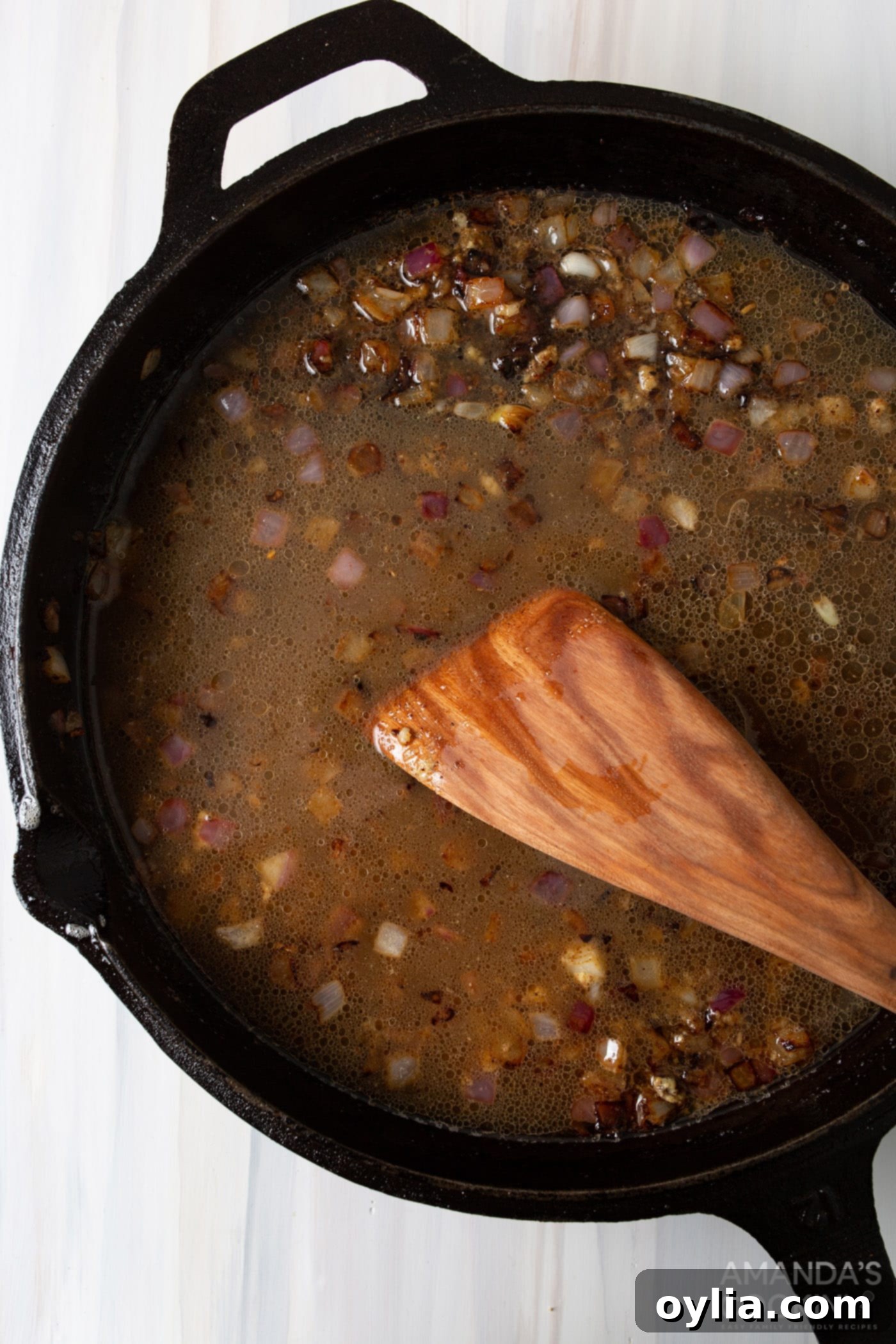 wood spatula stirring garlic into skillet with dressing ingredients