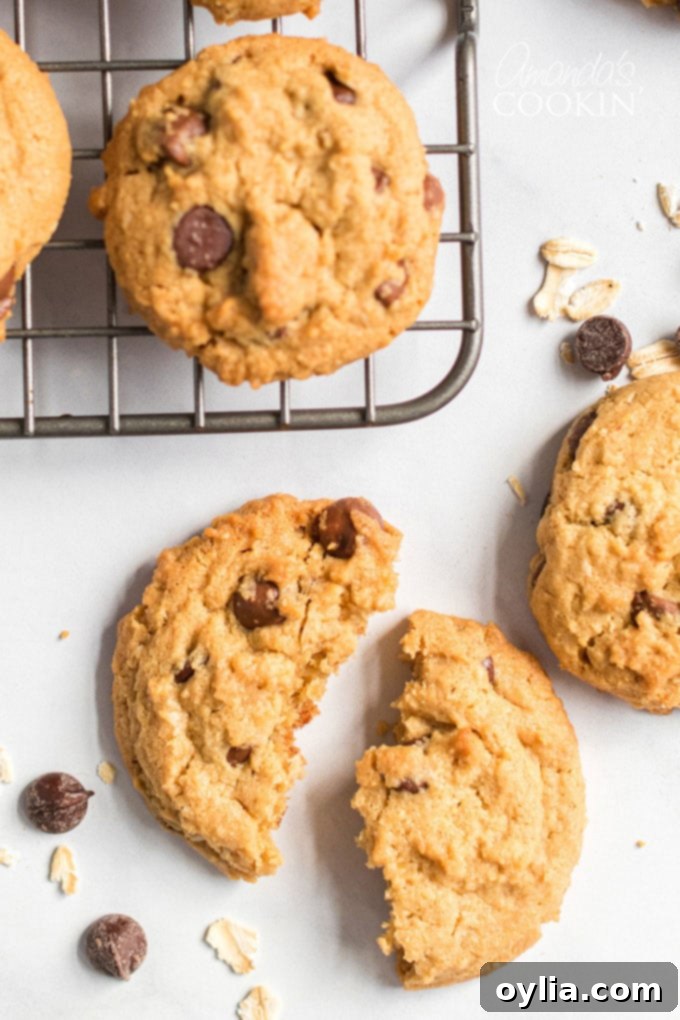 A broken peanut butter oatmeal chocolate chip cookie, with a chewy center, resting near a wire cooling rack.