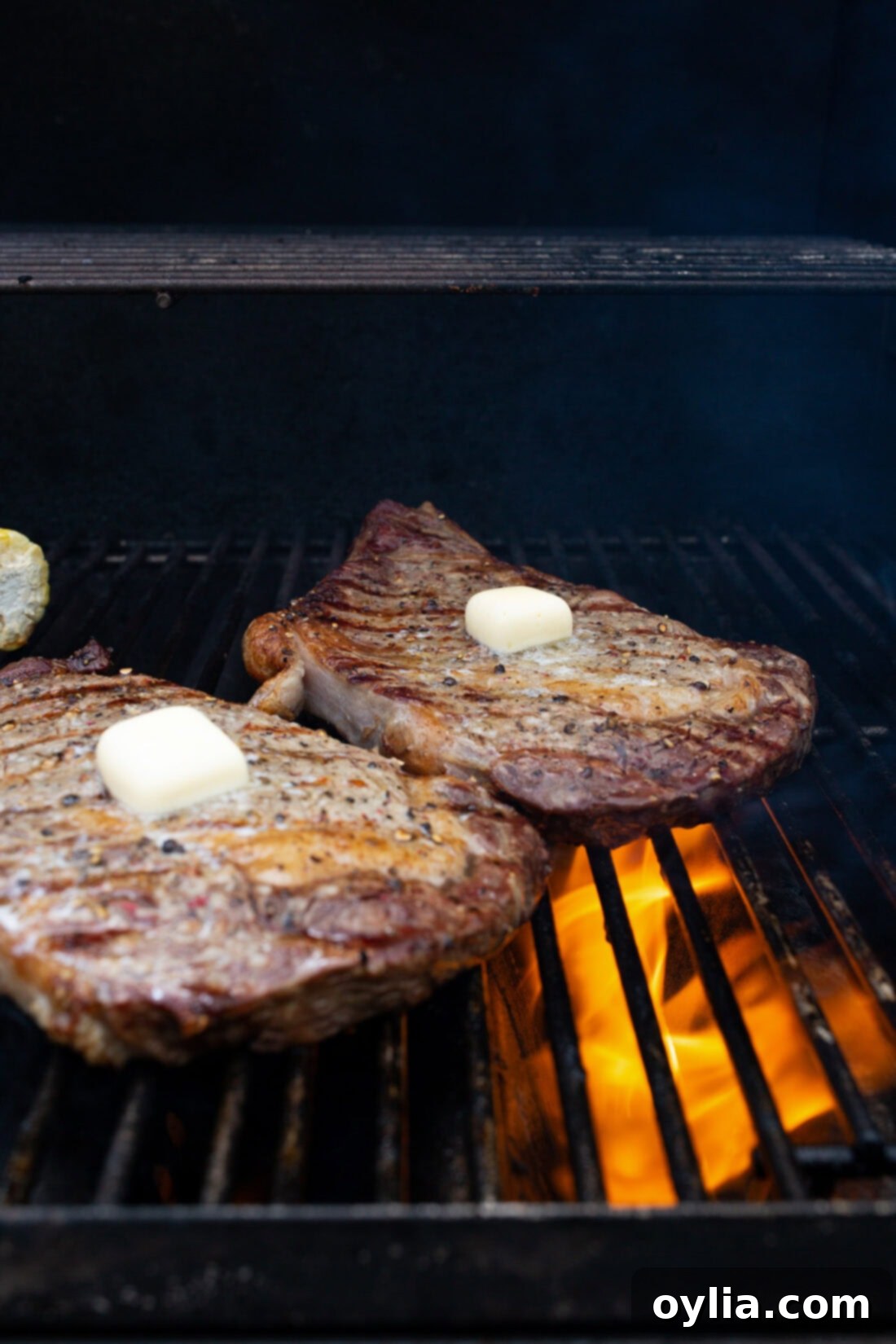 Sizzling Steak Perfection 3 Two New York strip steaks cooking on the grill, each topped with a pat of butter.