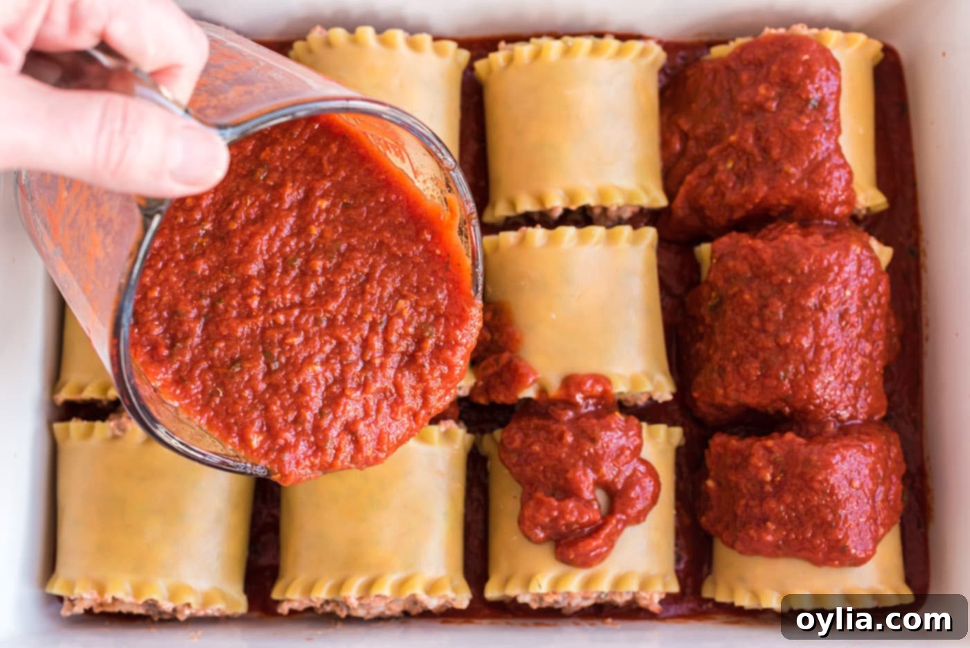 pouring sauce over lasagna roll ups in a dish