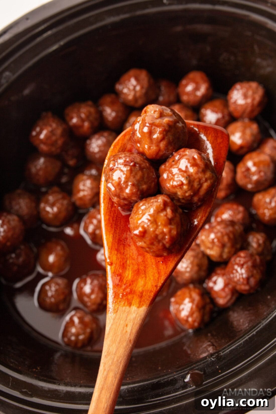 Sweet and Tangy Grape Jelly Meatballs 2 lifting appetizer meatballs from crockpot with wooden spoon
