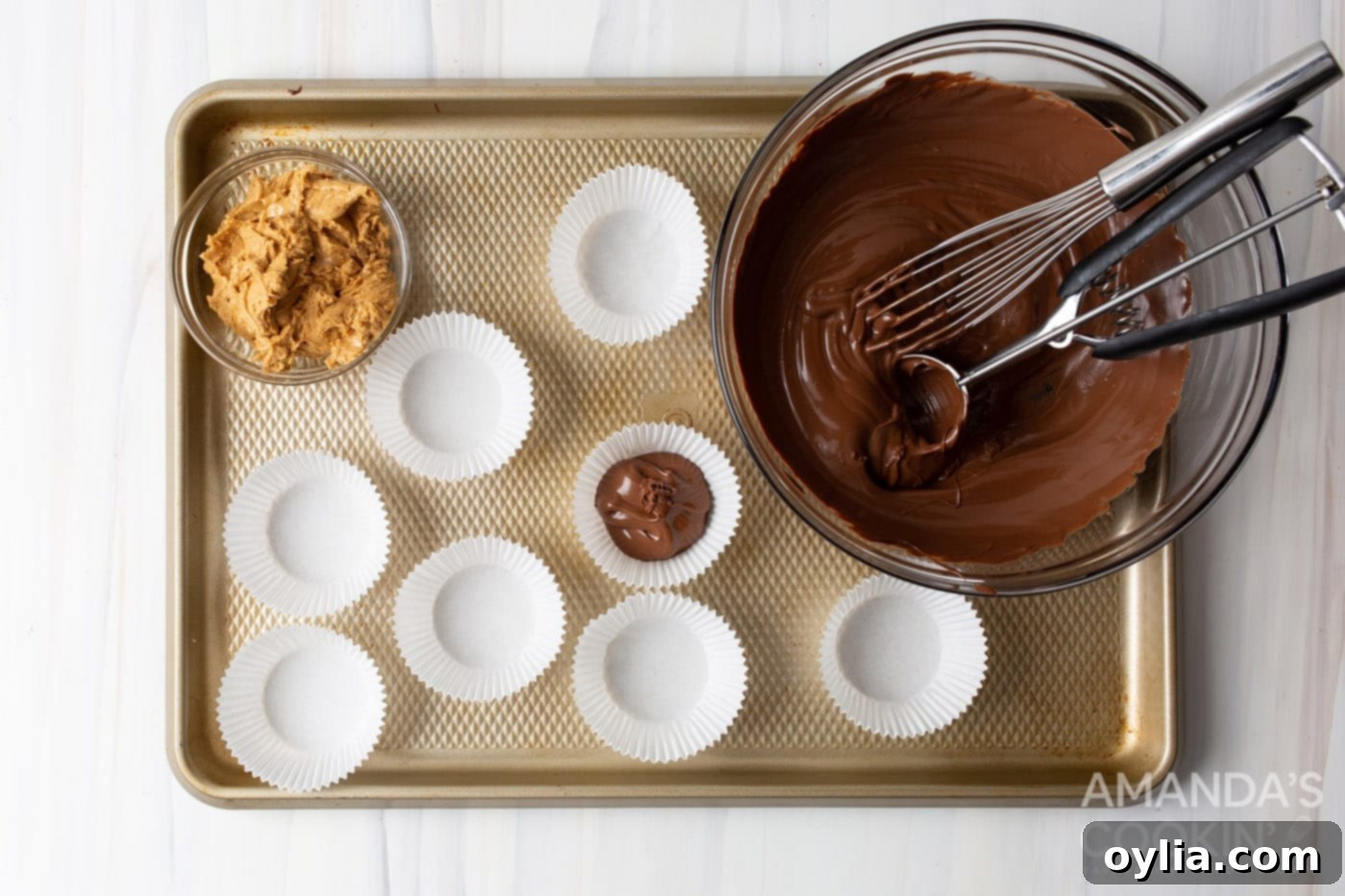 A spoonful of melted chocolate is placed into a cupcake liner, forming the base of the peanut butter cup.