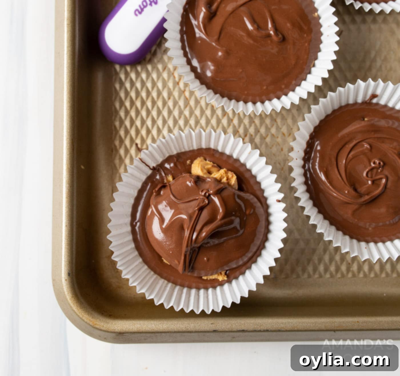 A cupcake liner fully filled with melted chocolate, covering the peanut butter center, smoothed on top.