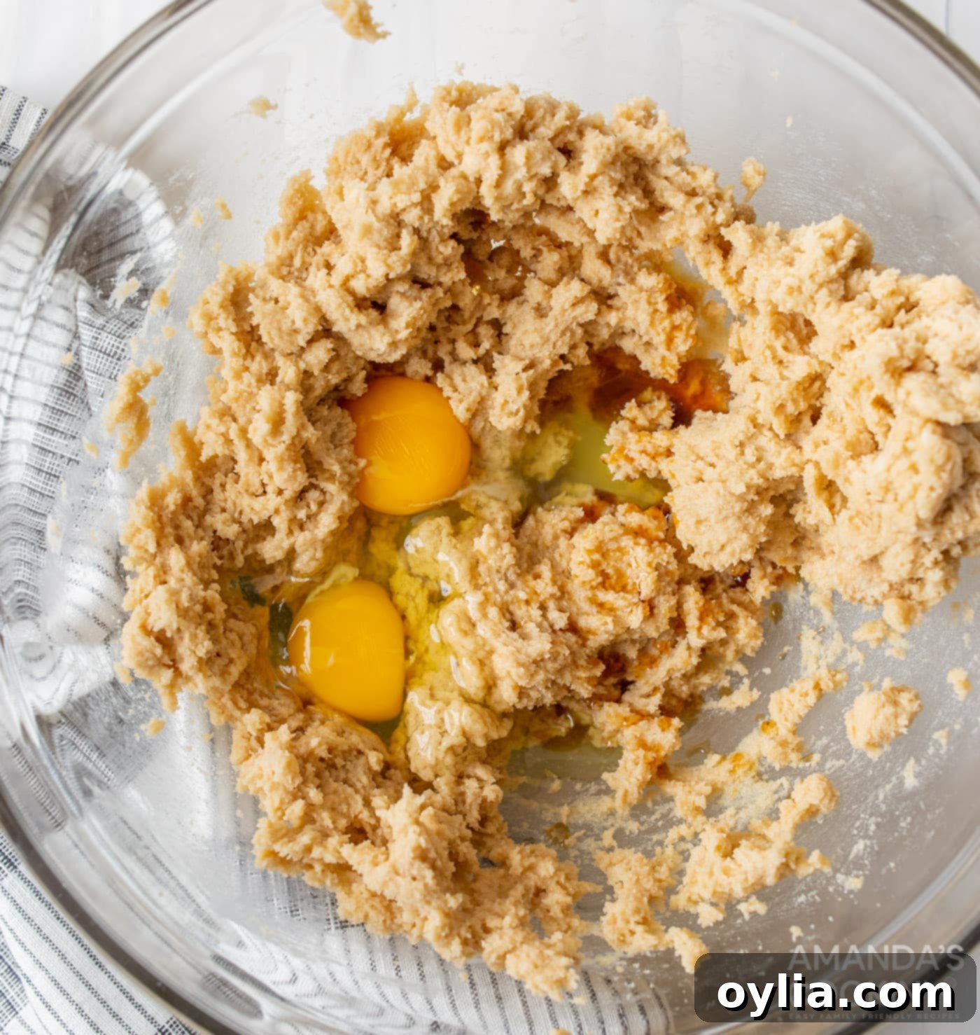 Cookie dough batter in a mixing bowl with eggs and vanilla extract being added
