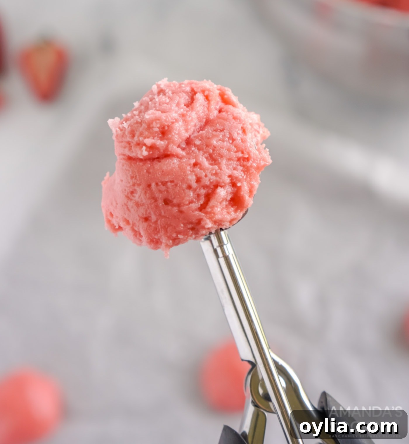 Strawberry cookie dough being scooped onto parchment paper with a cookie scoop.