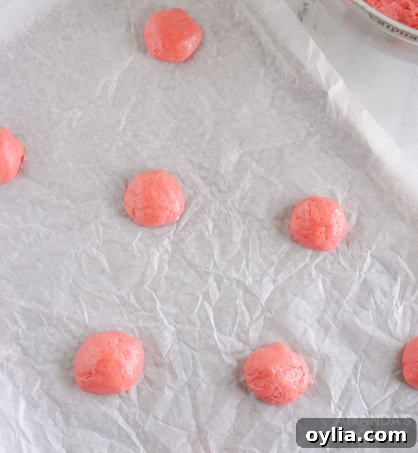 Strawberry cake mix cookies baking on parchment paper, edges just starting to brown.