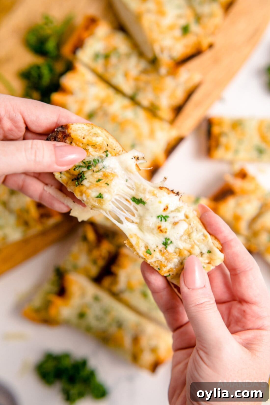 Pulling a piece of warm, golden Cheesy Garlic Bread apart with melted mozzarella stretching