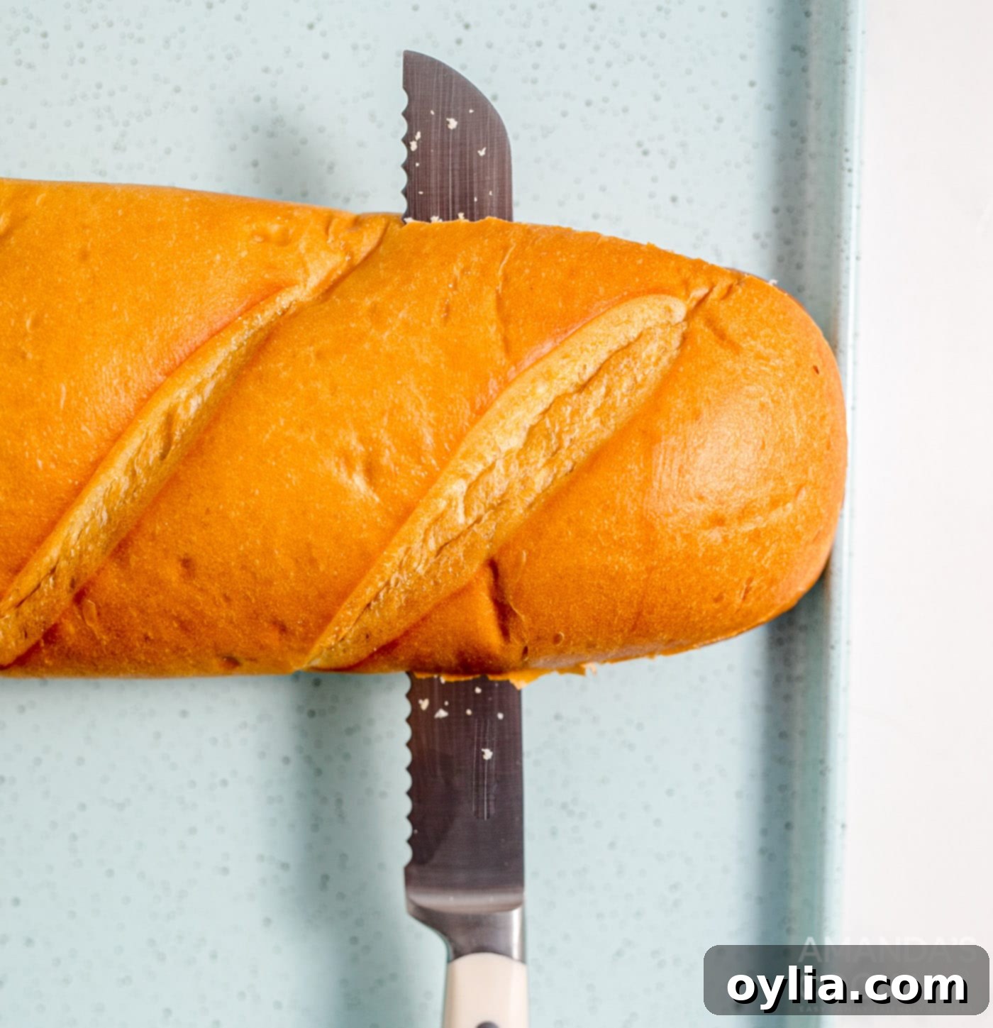 A knife expertly slicing a French bread loaf in half lengthwise