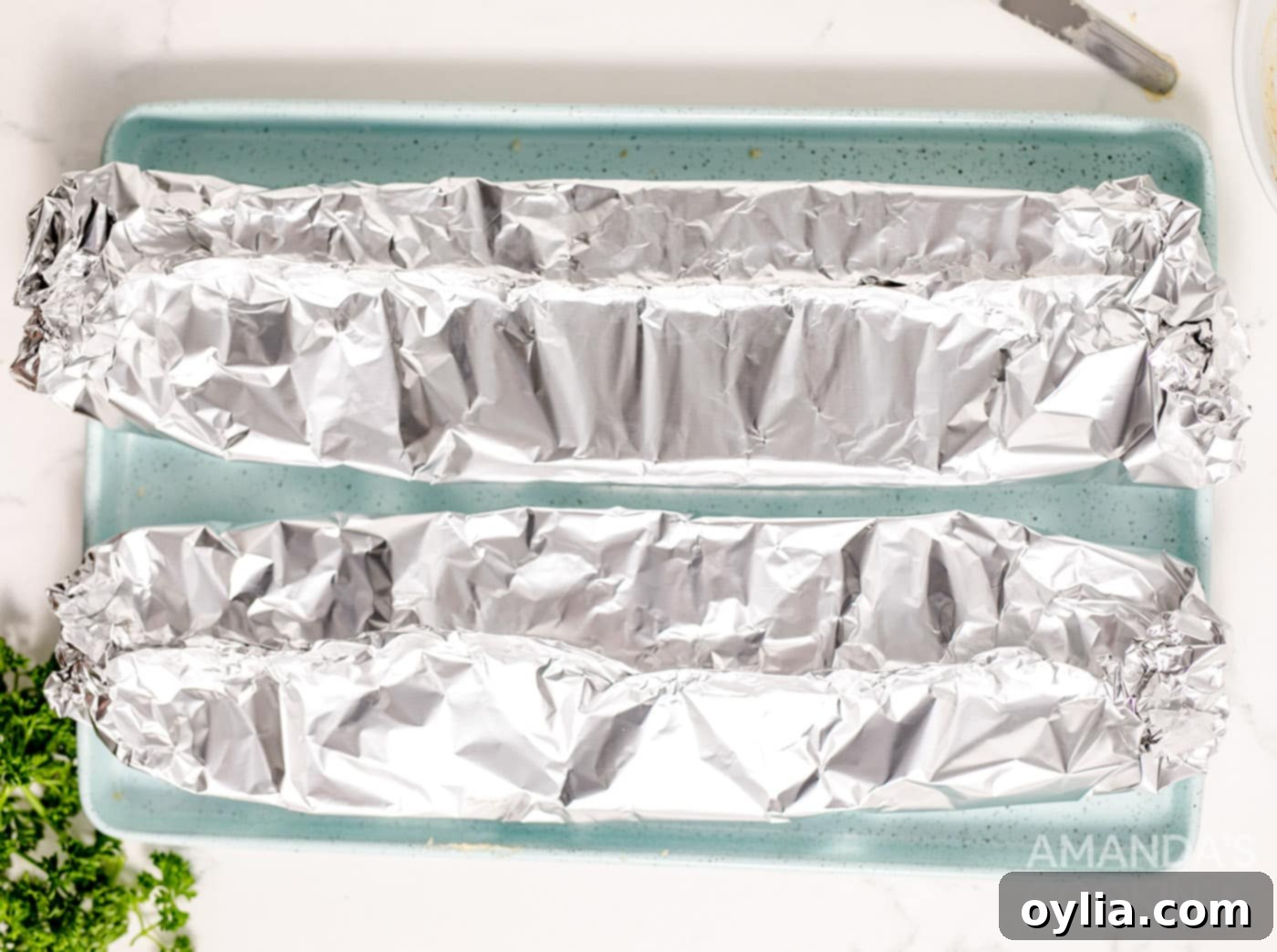 French bread loaves individually wrapped in aluminum foil on a baking sheet