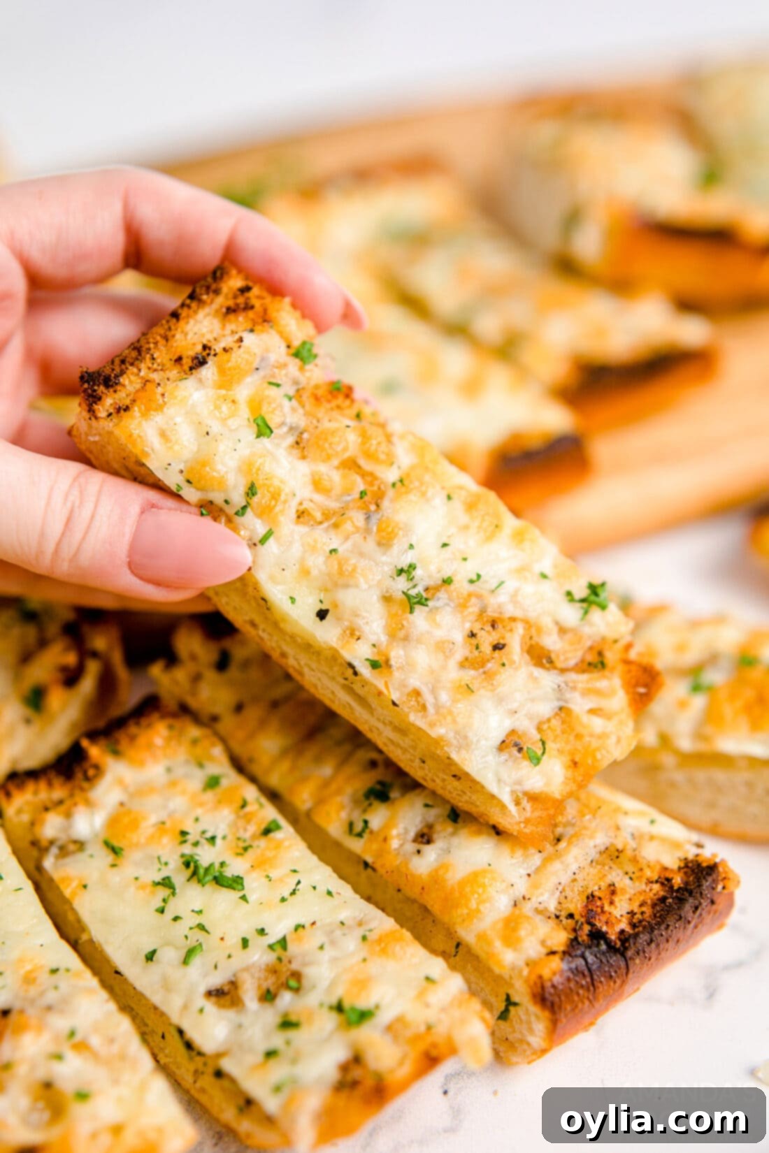 A hand reaching for a slice of golden-brown Cheesy Garlic Bread, highlighting its appealing texture