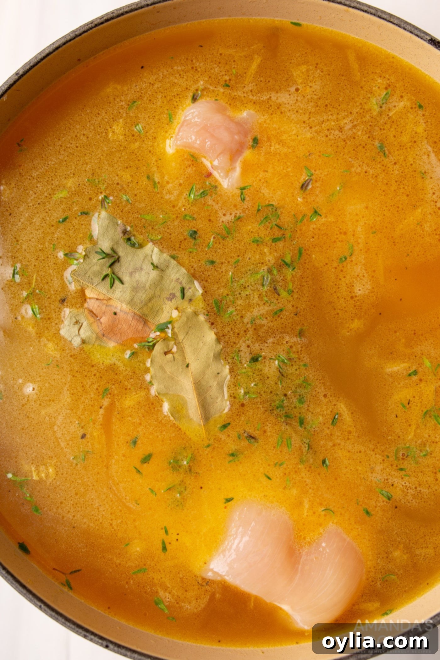 bay leaves, thyme, and raw chicken breasts simmering in chicken noodle soup broth