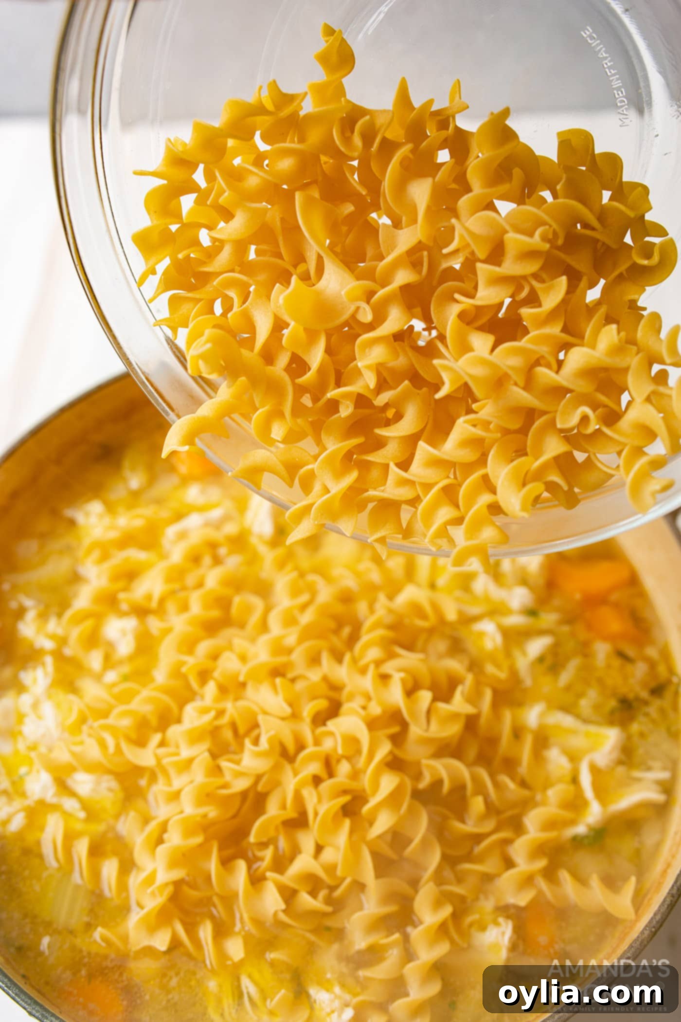 pouring egg noodles into chicken noodle soup broth with shredded chicken