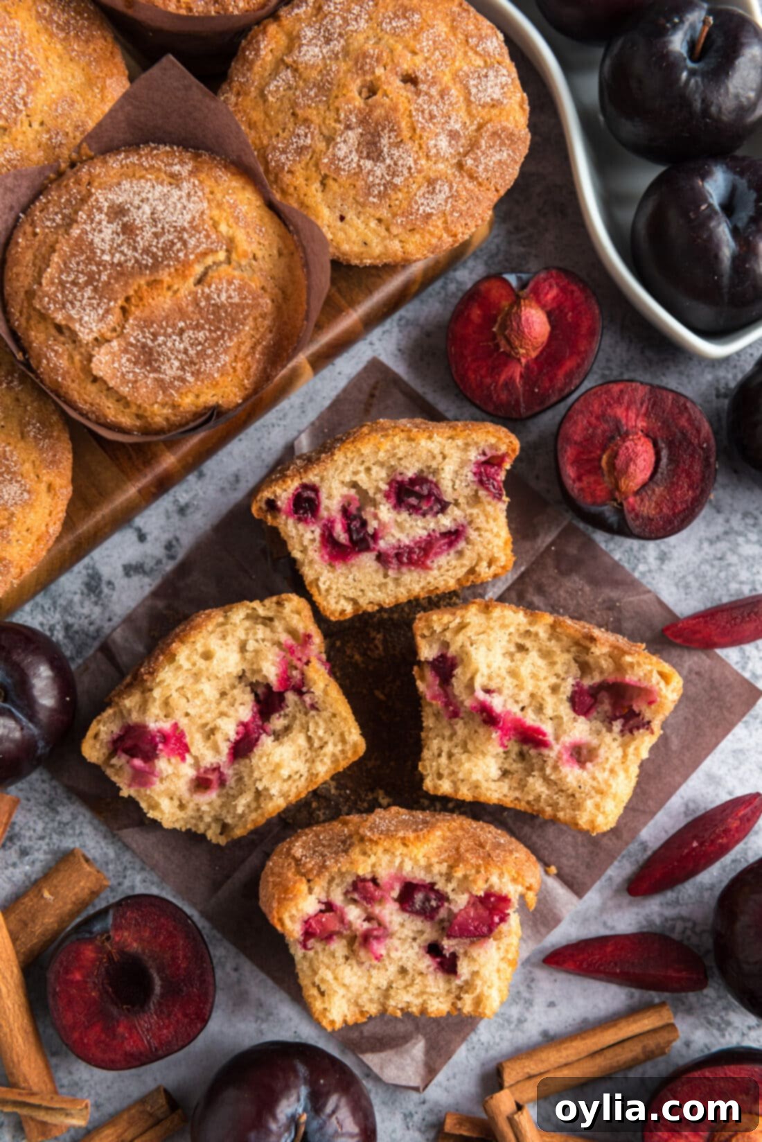 Two Sugar Crusted Plum Muffins cut in half on parchment paper, showcasing the juicy plum pieces inside and the golden sugar crust.