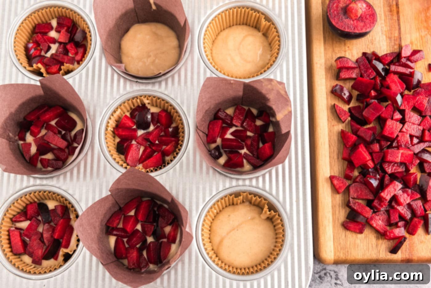 Adding small, diced pieces of fresh plums to muffin batter in a muffin pan.