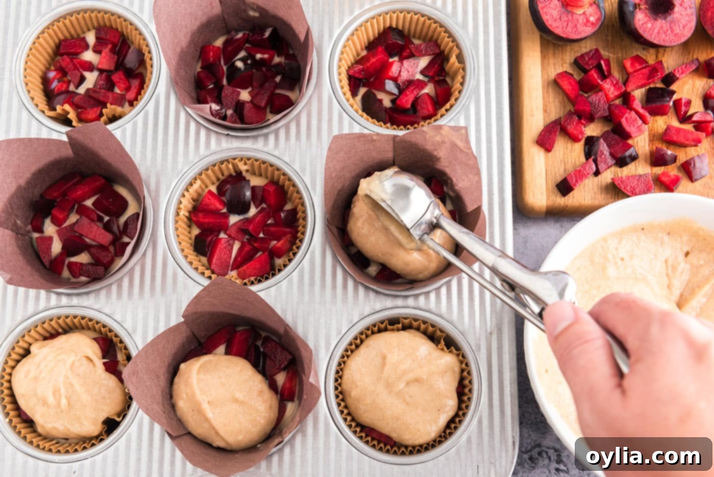 Scooping the remaining muffin batter over the layer of chopped plums in a muffin pan.