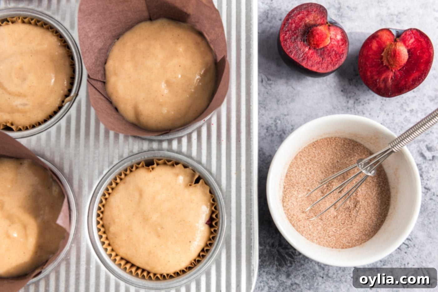 Small bowl of cinnamon sugar mixture placed next to a muffin pan filled with plum muffin batter, ready for topping.