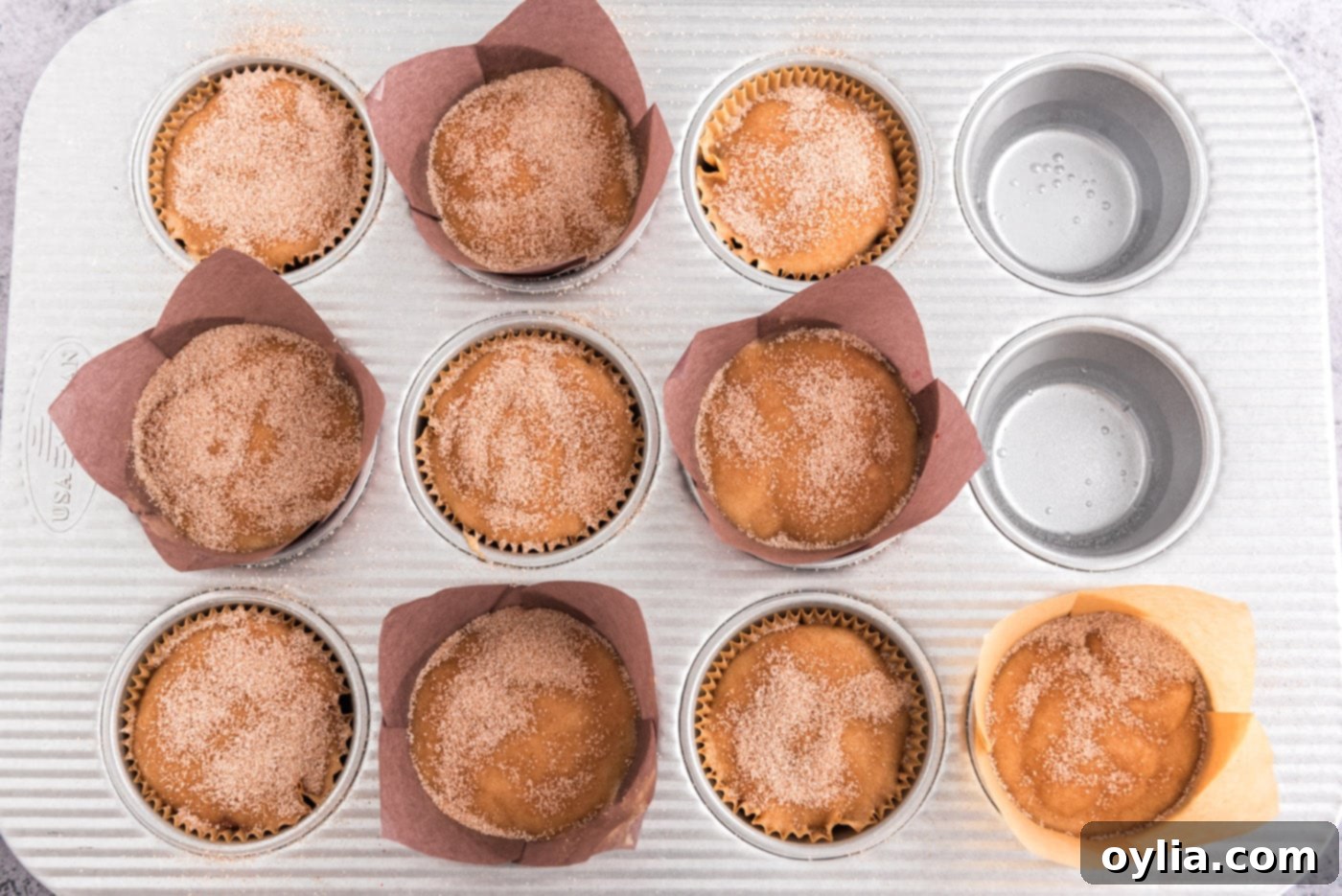 Plum muffin batter in a muffin pan generously topped with a cinnamon sugar mixture before baking.