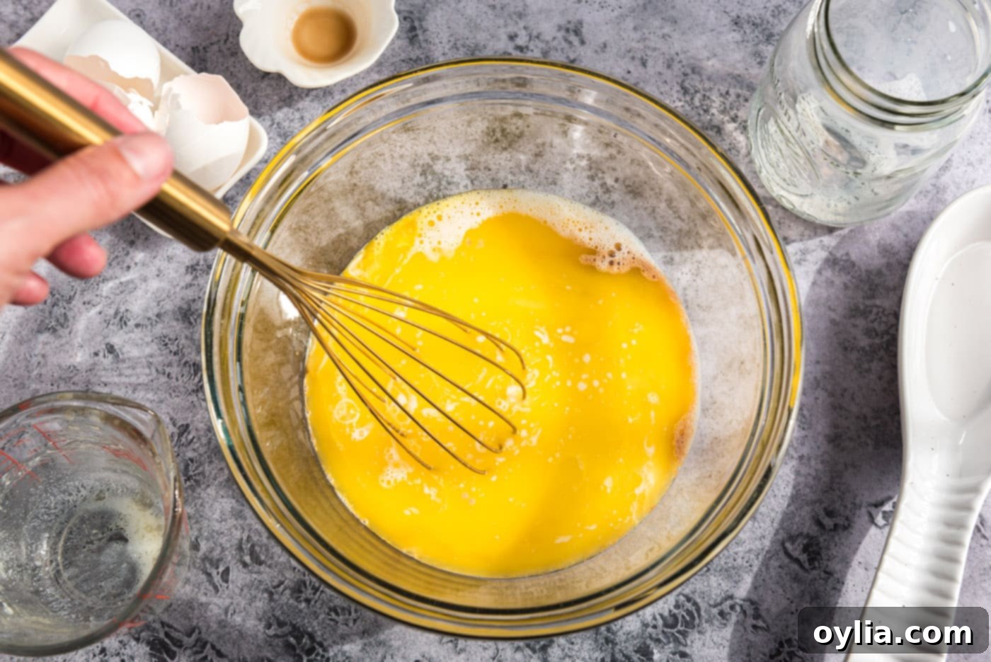 A hand whisking the egg, milk, vanilla, and melted butter mixture in a bowl until combined.