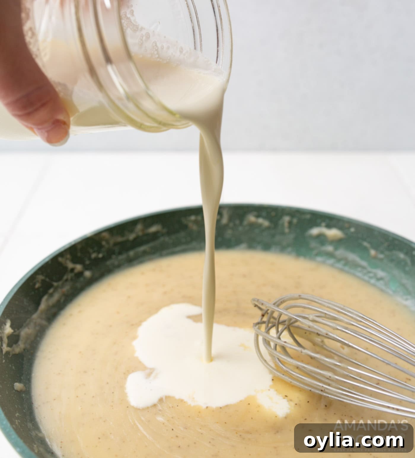 pouring heavy cream into cream of chicken soup over a skillet