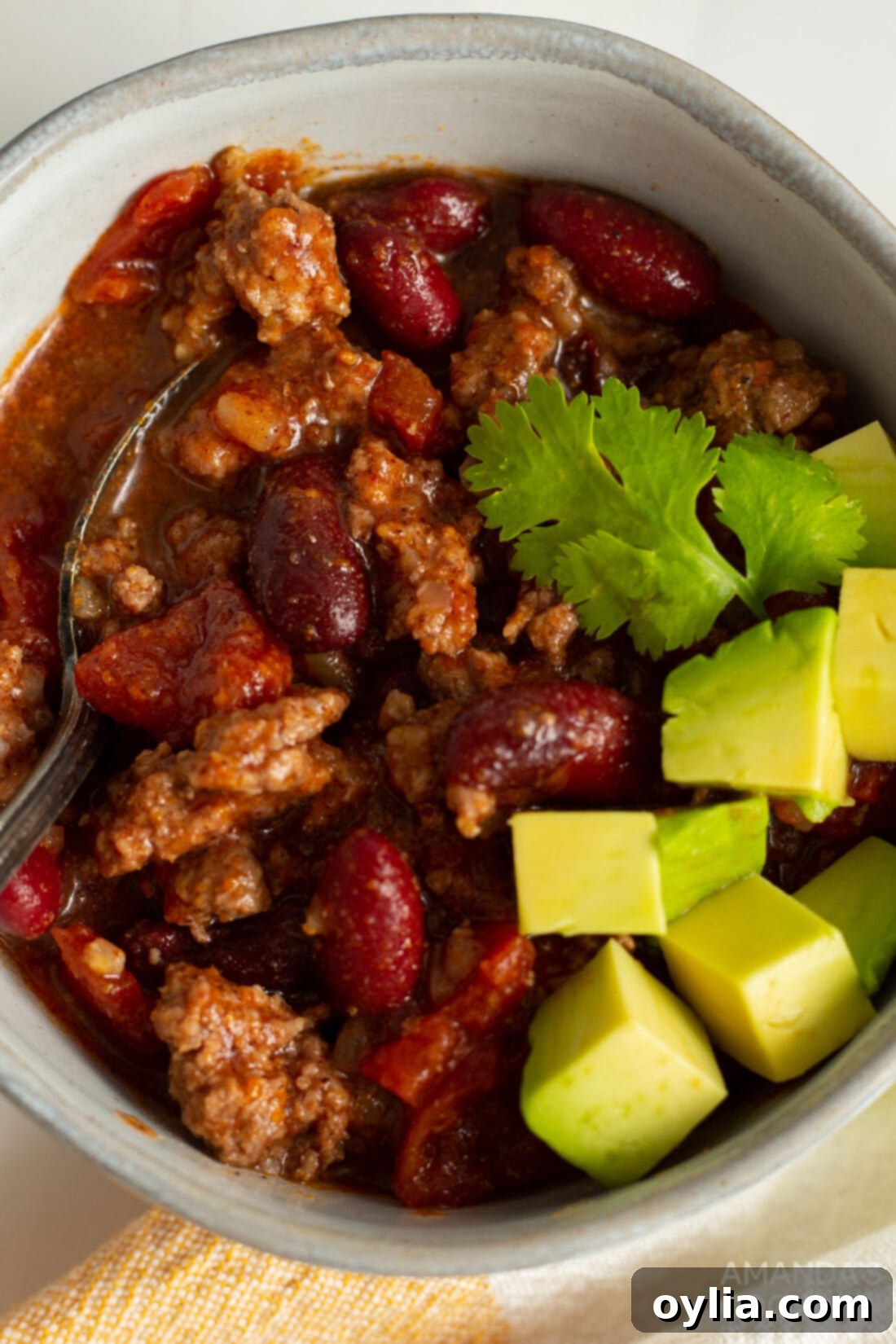 Slow Cooker Comfort Chili 3 A close-up of a rustic bowl filled with steaming Crockpot Chili, generously topped with a dollop of cool sour cream, a sprinkle of fresh green onions, and some shredded cheese, showcasing its inviting texture.