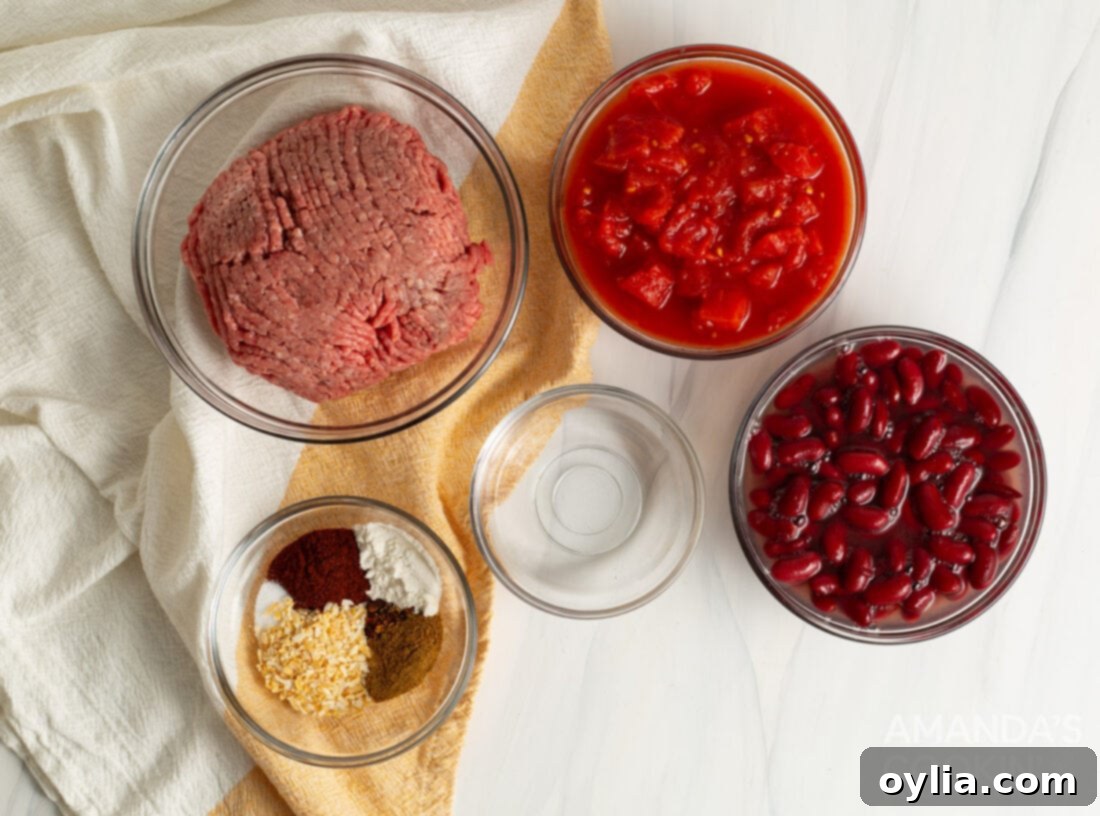 Slow Cooker Comfort Chili 4 A vibrant spread of fresh ingredients for Crockpot Chili, including raw ground beef, canned red kidney beans, diced tomatoes, a variety of spices in small bowls, and other essentials, arranged on a kitchen counter.