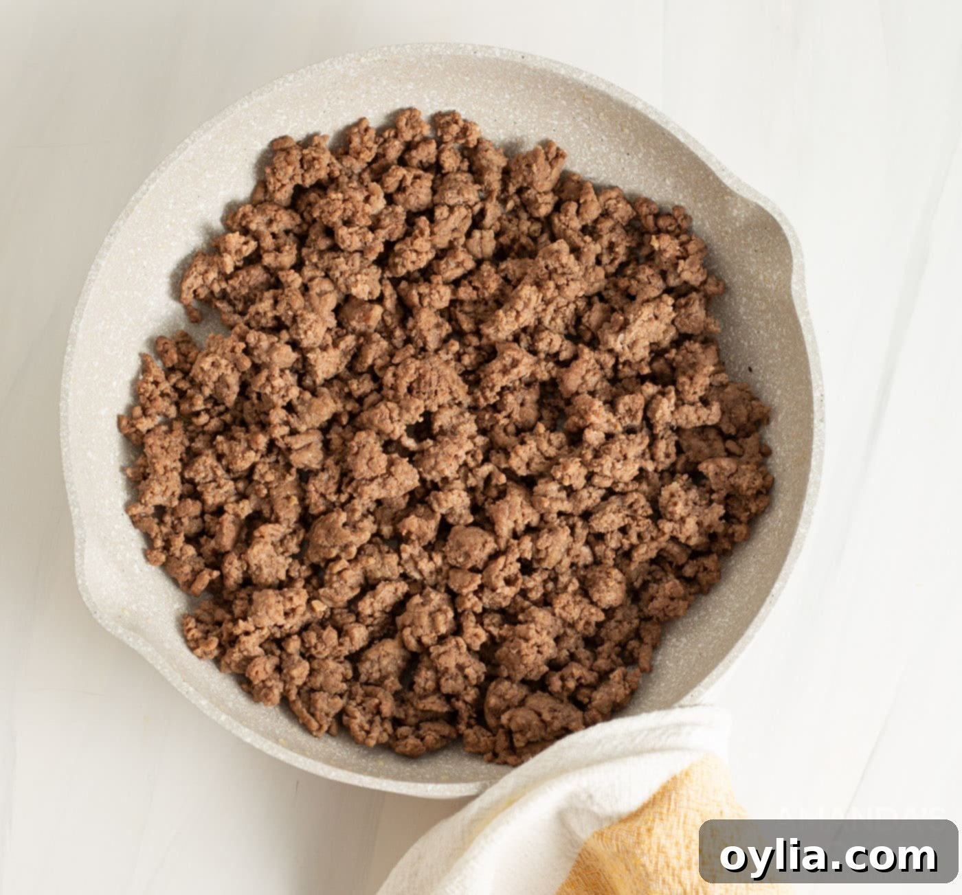 A close-up image of perfectly browned ground beef in a metal strainer, with excess fat visibly draining away, ready to be added to the crockpot.