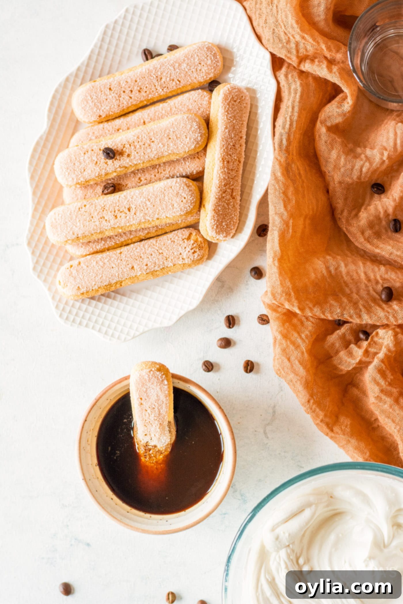 A ladyfinger being quickly dipped into a bowl of espresso coffee, ready for tiramisu layering.