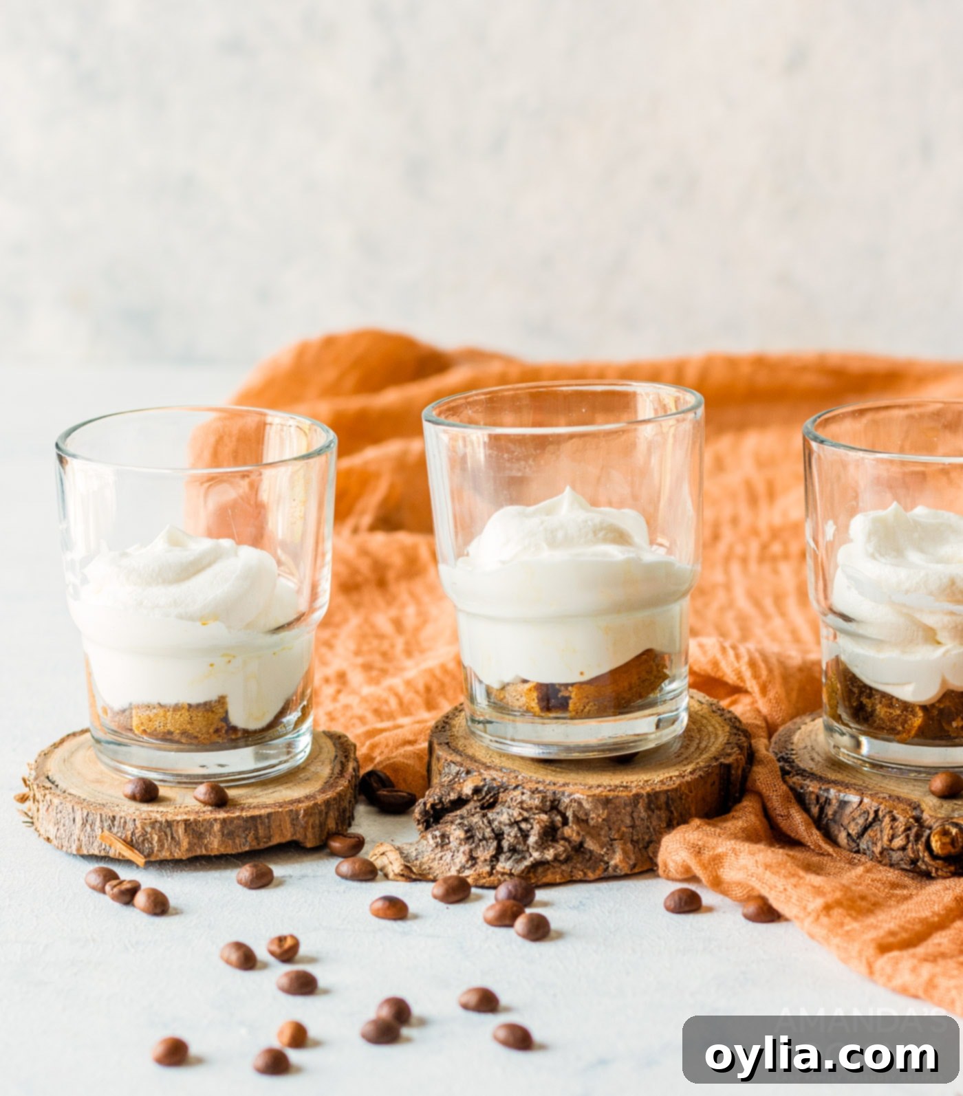 Multiple individual tiramisu trifles being layered with mascarpone cream and ladyfingers.