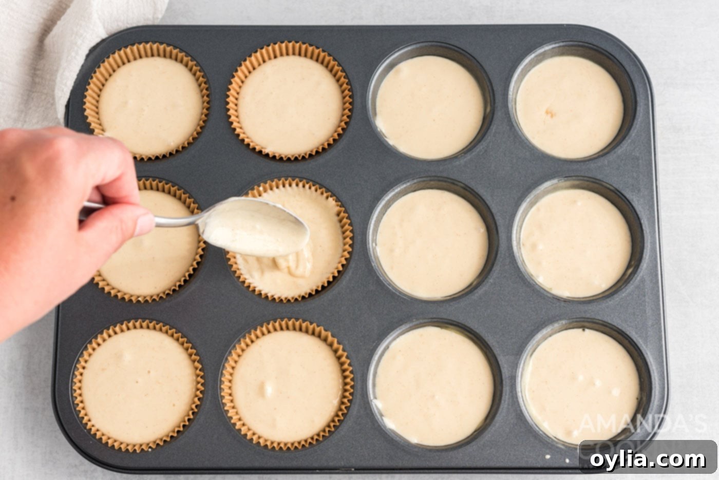 Cupcake batter being scooped into lined muffin cups, filling them about three-quarters full.