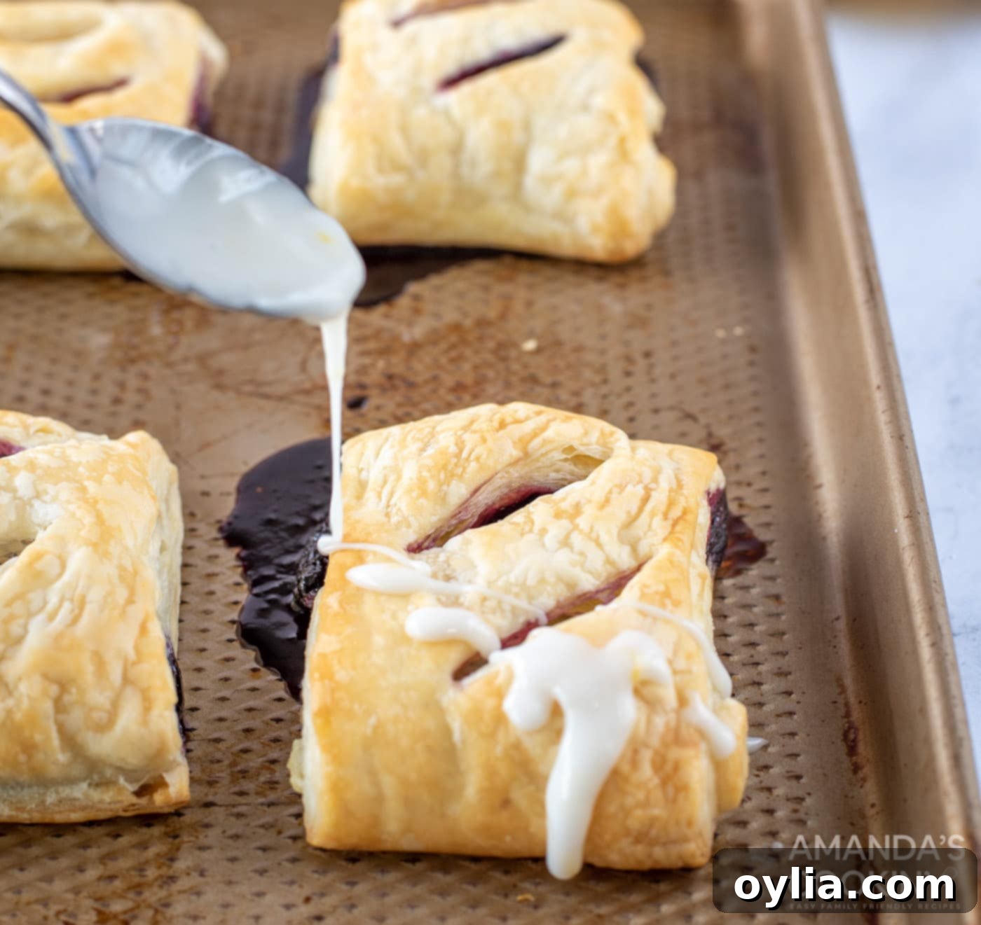 Spoon drizzling lemon glaze onto cooled lemon blueberry hand pies