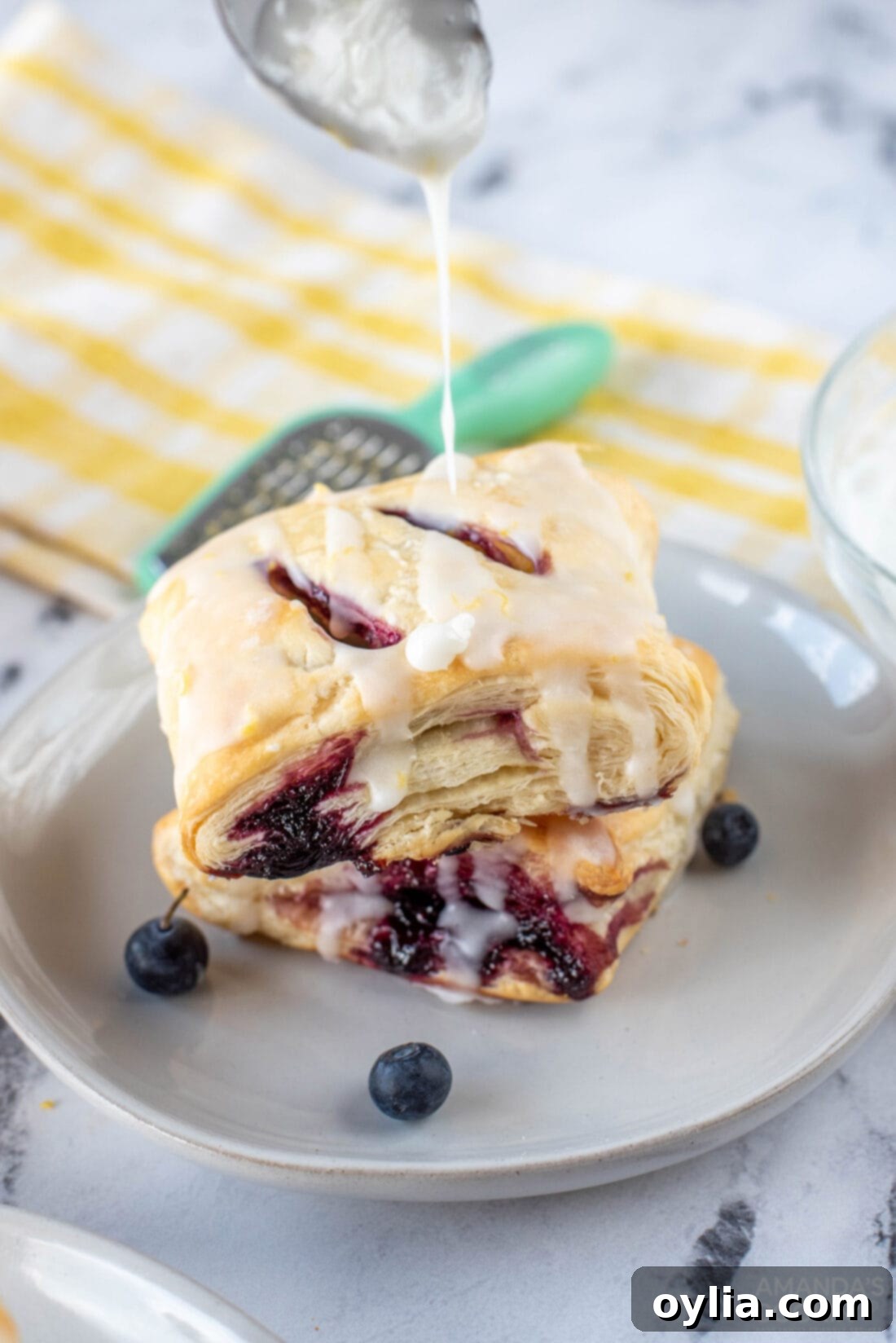 Close-up of lemon glaze being drizzled onto a stack of Lemon Blueberry Croissant Hand Pies