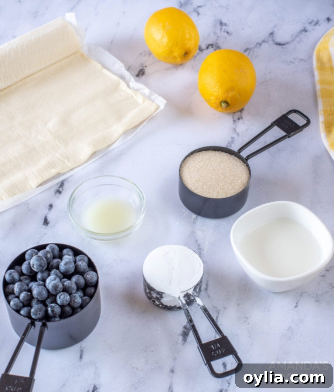 Ingredients laid out for making Lemon Blueberry Croissant Hand Pies, including puff pastry, blueberries, lemons, and sugar