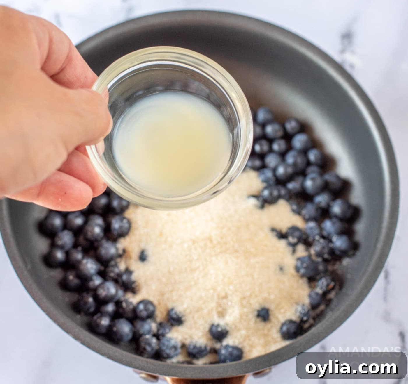 Pouring lemon juice into the blueberry and sugar mixture in a saucepan