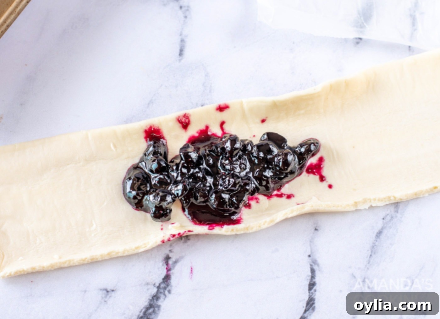 Scooping blueberry mixture onto the center of a pastry dough rectangle