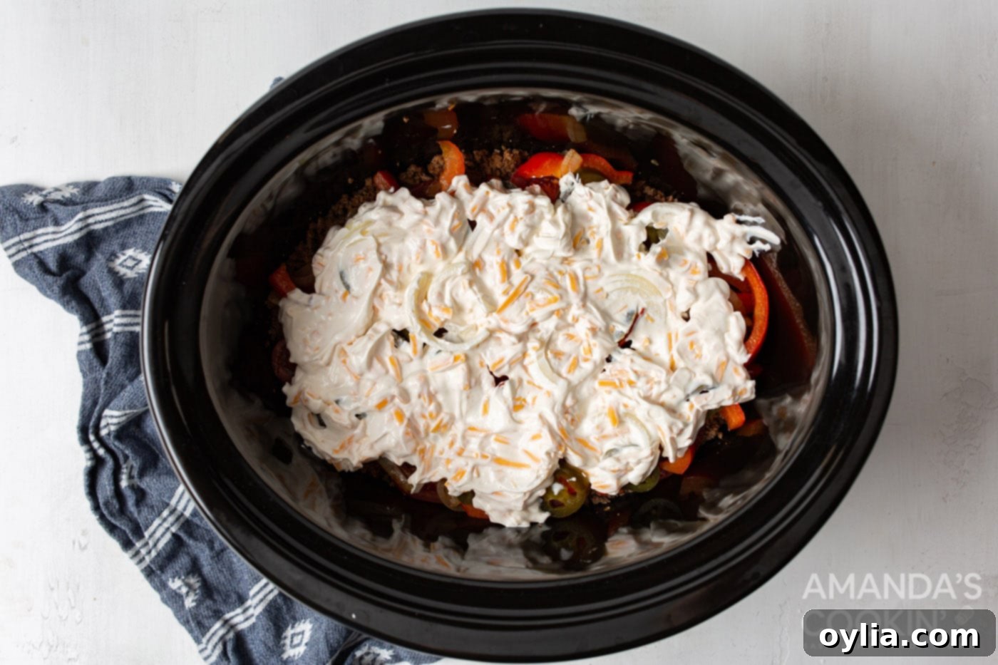sour cream mixture on top of ground beef and veggies in slow cooker