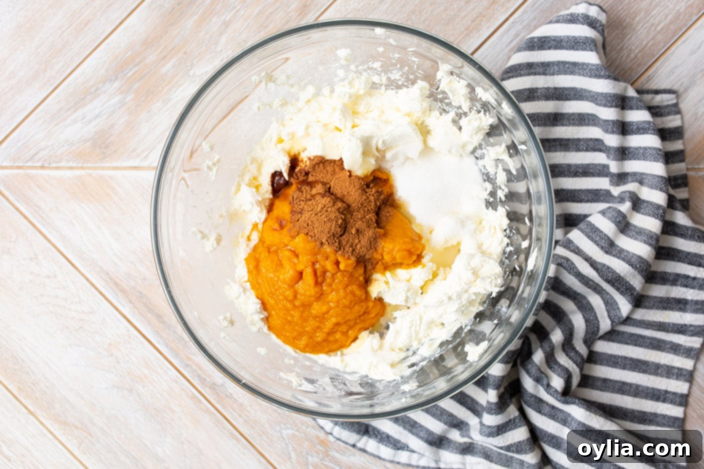 Cream cheese, pumpkin puree, pie spice, and vanilla extract are being mixed in a bowl with a hand mixer.