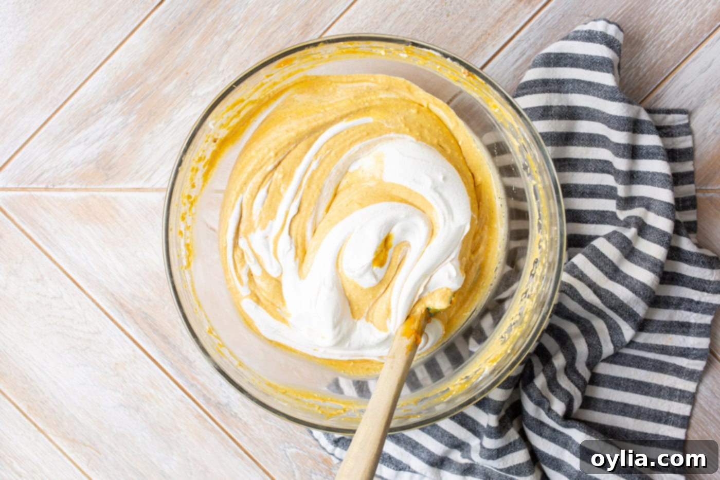 Whipped topping is gently folded into the pumpkin cheesecake mixture in a bowl.