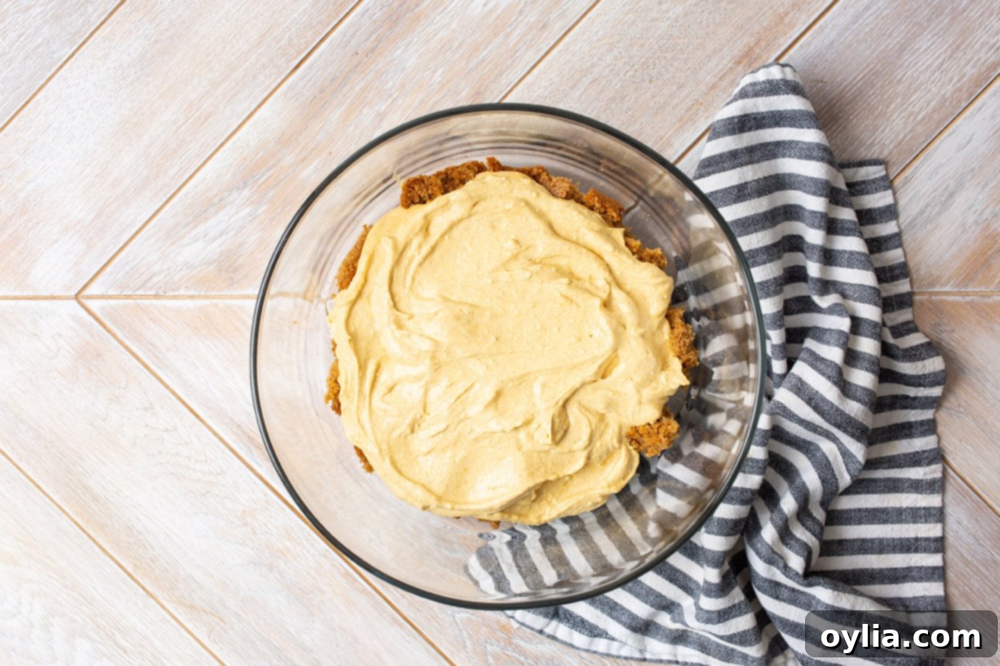 A smooth layer of pumpkin cheesecake mixture is spread over the crumbled gingerbread cake in the trifle dish.
