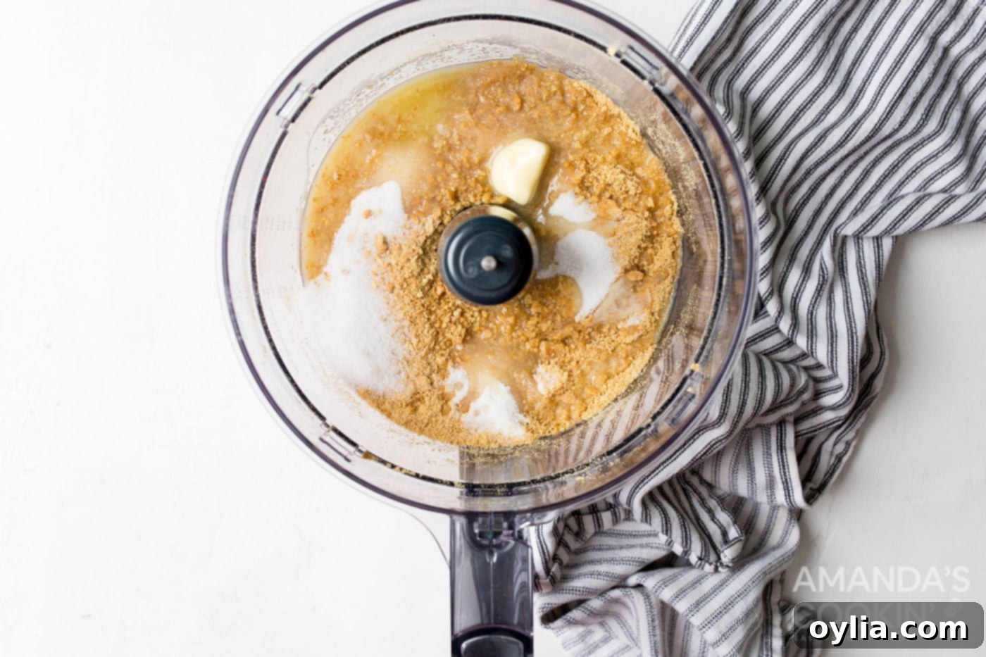 Graham cracker crumbs, sugar, melted butter, and a pinch of salt being pulsed in a food processor for the cheesecake crust
