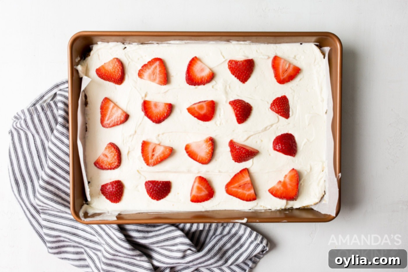 Finished No Bake Cheesecake Bars topped with vibrant red sliced strawberries, chilling in a baking dish