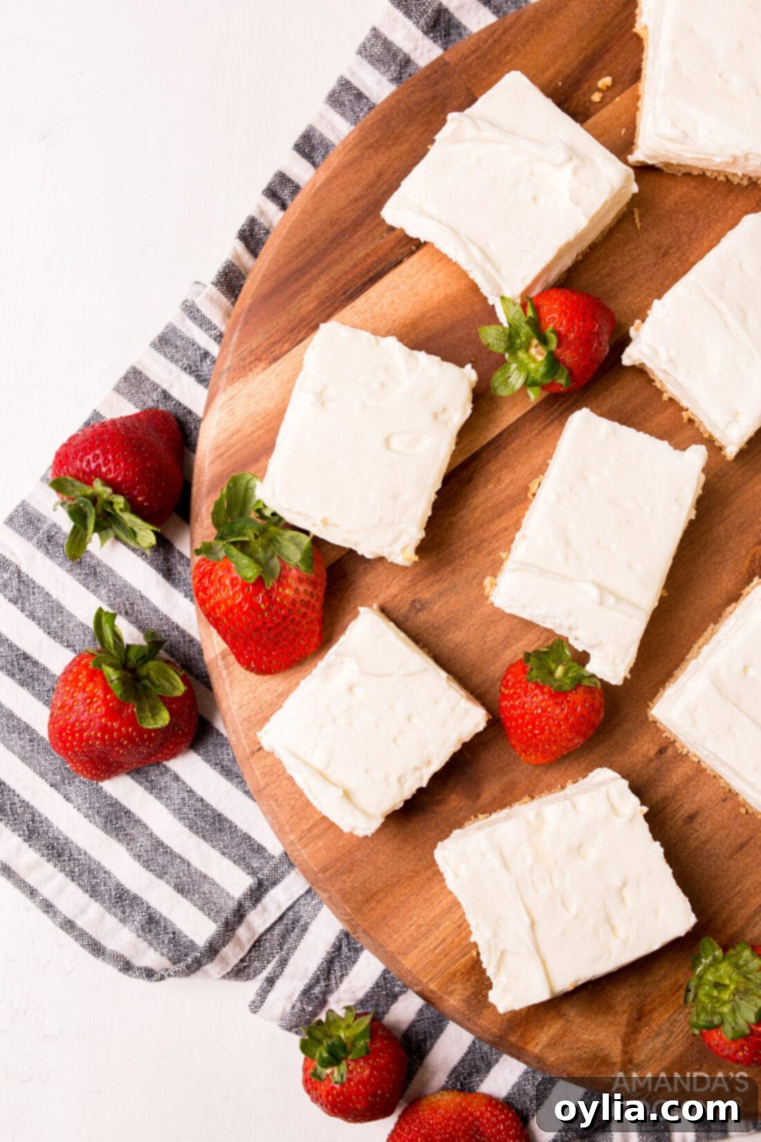 Overhead view of a tray of perfectly set No Bake Cheesecake Bars, some topped with strawberries, highlighting their creamy texture and golden crust