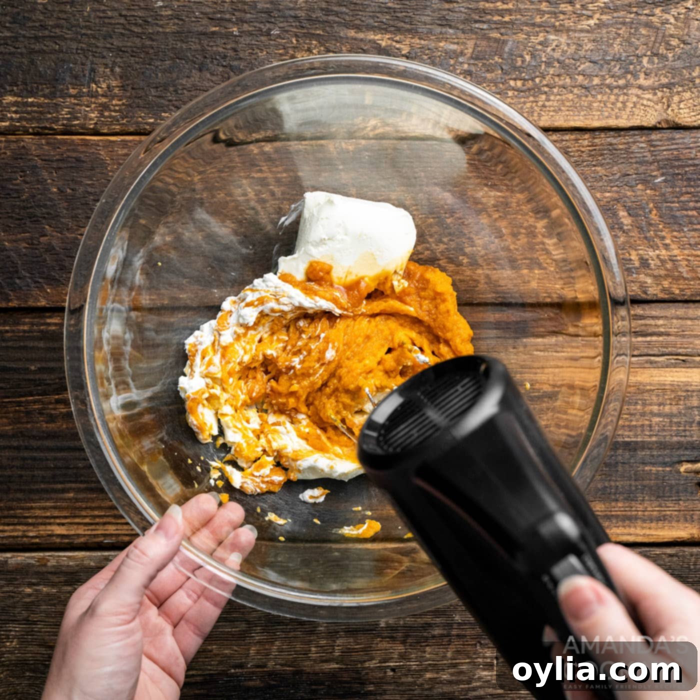 Using a hand mixer to beat together pumpkin puree and cream cheese in a large bowl, showing the initial mixing step for the dip.