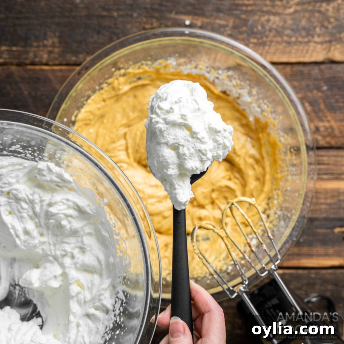 A spoonful of whipped cream being added to the pumpkin cream cheese mixture, ready for initial blending.